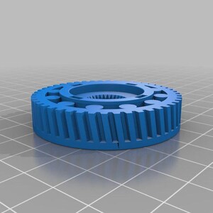 Op de afbeelding: Een blauw cirkelvormig tandwiel met een reeks verticale tanden langs de buitenrand en een centrale naaf met interne spiebanen. Het object heeft een plat bovenoppervlak met een ring van cirkelvormige inkepingen rond de centrale opening.