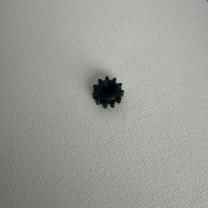 May include: A small, black, circular gear component featuring twelve distinct teeth around its outer perimeter and a hollow, cylindrical center opening, designed for mechanical assembly and rotational movement applications.