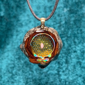 May include: A unique pendant necklace featuring a detailed design. The pendant has a brown, gray, and gold outer layer, with a central design of a geometric pattern and a rainbow-colored skull. The necklace is suspended from a dark brown cord.