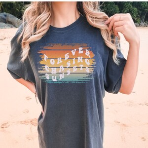 May include: A dark gray t-shirt with a colorful graphic design that reads "FOREVER CHASING SUNSETS".