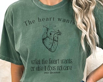 May include: Green t-shirt with a vintage look featuring a black and white illustration of a heart and the text "The heart wants what the heart wants or else it does not care" and "EMILY DICKINSON".