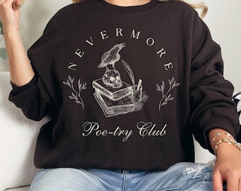May include: A dark brown sweatshirt with the words "NEVERMORE Poetry Club" in a circular design. The design includes a raven, skull, books, and quill pen. The sweatshirt is a long-sleeved, crew neck style.