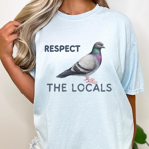 May include: Light blue t-shirt with a graphic of a pigeon and the text "Respect the Locals".