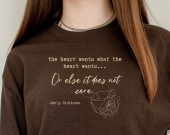 May include: A brown t-shirt with a quote printed on it: "the heart wants what the heart wants... Or else it does not care." - Emily Dickinson. The quote is printed in a light brown color and is accompanied by a line drawing of a rose.