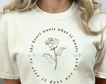 May include: A white t-shirt with a brown floral design and the text "The heart wants what it wants, so else it does not care" by Emily Dickinson.
