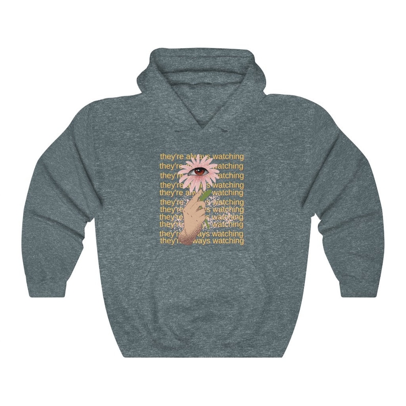 May include: A dark gray hoodie with a pink flower with an eye in the center. The text "they're always watching" is repeated multiple times in yellow.