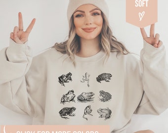 May include: A beige sweatshirt with a graphic print of nine frogs in black and white. The text "SUPER SOFT" is on a pink background in the top right corner of the image. The text "CLICK FOR MORE COLORS" is at the bottom of the image.