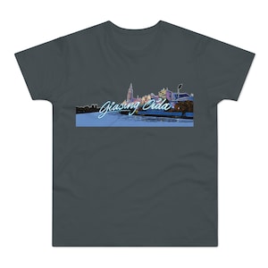 Könnte beinhalten: Ein dunkelgraues T-Shirt mit einem Stadtbild-Motiv und dem Text "Giasng Oda" in blauer Neon-Schrift.