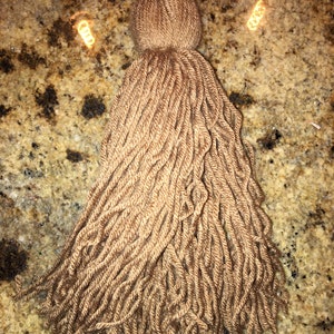 Könnte beinhalten: Ein brauner Quaste aus Garn. Die Quaste ist etwa 25 cm lang und hat eine dicke, flauschige Textur.