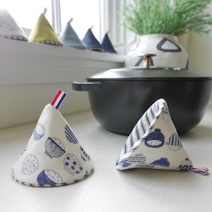May include: Two white fabric pot holders with blue and white patterns. One pot holder has a blue and white striped pattern and the other has a pattern of blue bowls with white rice. Both pot holders are in the shape of a cone.