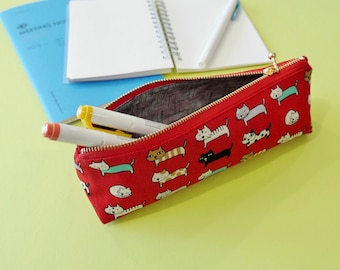 May include: Red zippered pencil case with a repeating pattern of colorful cats. The case is open and has two white and yellow markers inside.