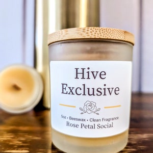 May include: A glass candle jar with a bamboo lid. The candle is labeled "Hive Exclusive" and "Rose Petal Social". The candle is 5 oz and made with beeswax.
