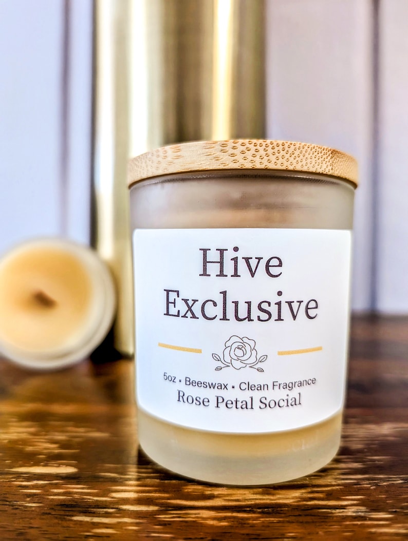 May include: A glass candle jar with a bamboo lid. The candle is labeled "Hive Exclusive" and "Rose Petal Social". The candle is 5 oz and made with beeswax.