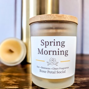 May include: A frosted glass candle jar with a wooden lid. The label reads "Spring Morning" and "5oz Beeswax Clean Fragrance Rose Petal Social".