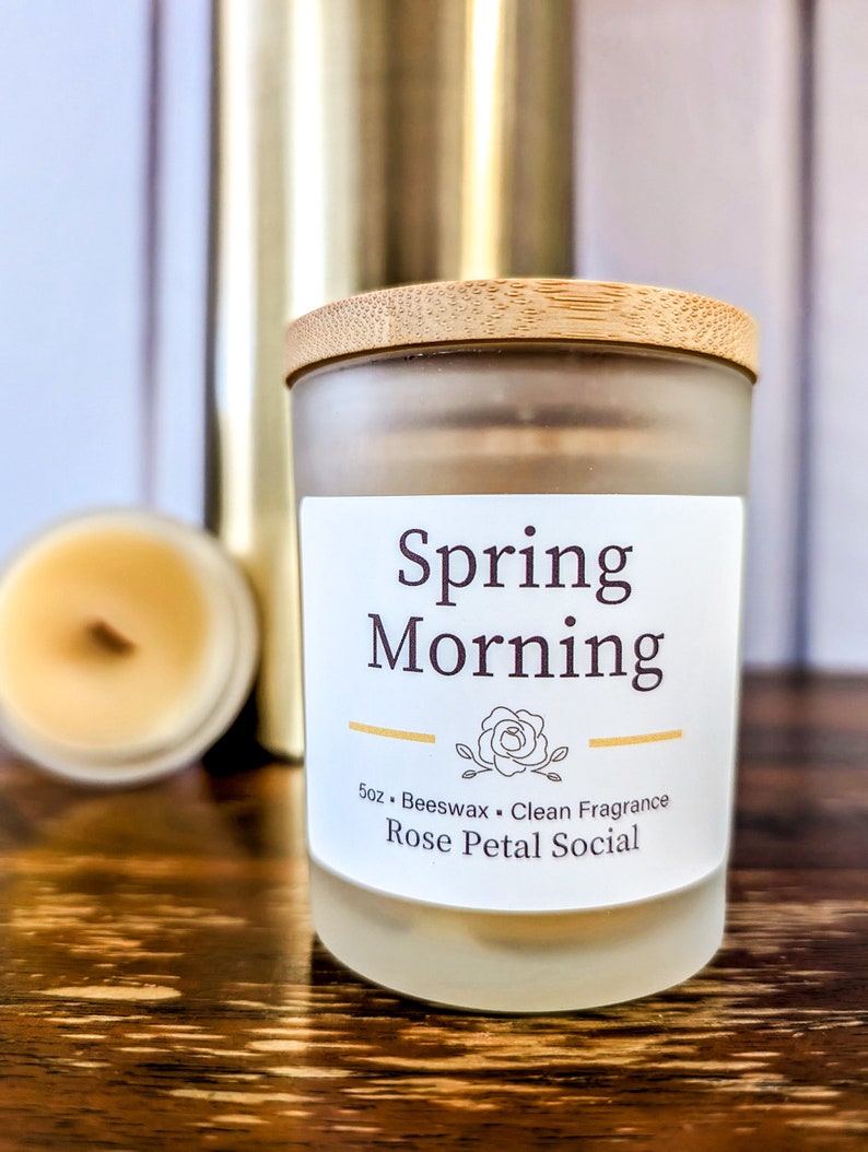 May include: A frosted glass candle jar with a wooden lid. The label reads "Spring Morning" and "5oz Beeswax Clean Fragrance Rose Petal Social".