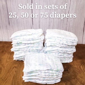 May include: Three stacks of white nappies with a green and purple design. The text "Sold in sets of 25, 50 or 75 diapers" is at the top of the image.