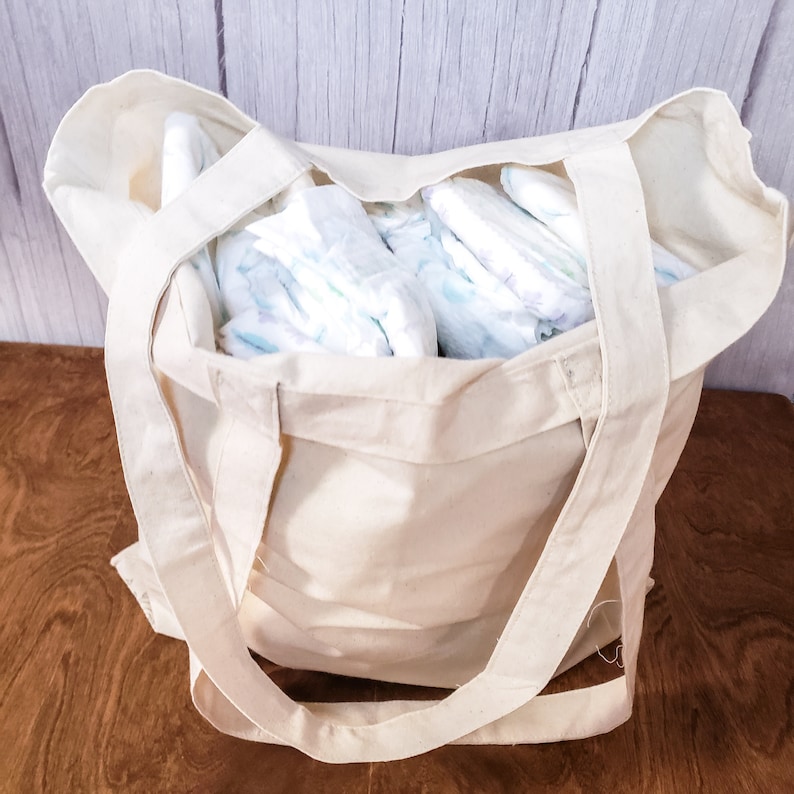 May include: A white canvas tote bag filled with a stack of white and blue baby nappies.
