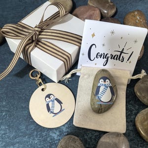 Arte único de guijarros naturales con un pingüino feliz en una bufanda: set de regalo personalizado con adorno colgante, tarjeta de felicitación y caja de regalo.
