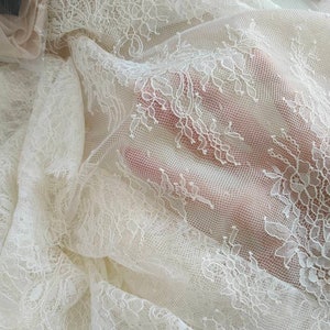 May include: White lace fabric with a delicate floral pattern. The lace is sheer and has a soft, flowing texture.