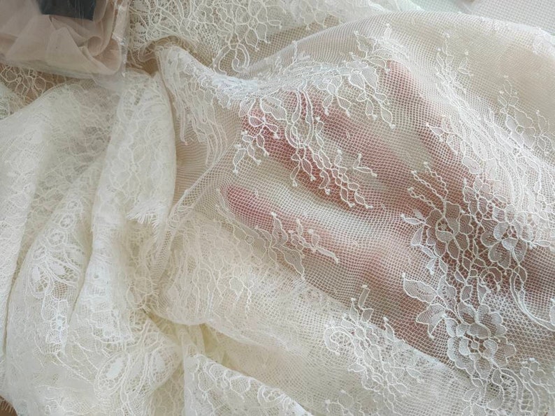 May include: White lace fabric with a delicate floral pattern. The lace is sheer and has a soft, flowing texture.