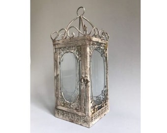 May include: A white metal lantern with a decorative scrolled design and glass panels. The lantern has a distressed finish and is perfect for adding a touch of rustic charm to any home.