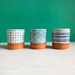 May include: Three ceramic plant pots with terracotta bases and blue and white patterned designs. The patterns include circles, zigzags, and triangles. The pots are set against a teal background.
