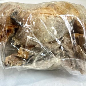 May include: A clear plastic bag filled with dried fish. The fish pieces are various shades of brown and tan, with some darker areas. The bag is sealed, and the contents are visible through the transparent material.