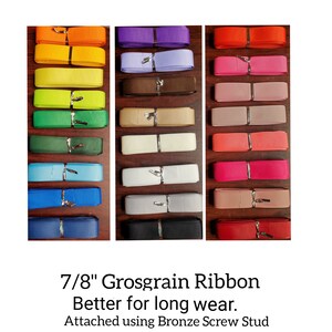 K&ouml;nnte beinhalten: Eine Auswahl an 2,2 cm breiten Grosgrain-B&auml;ndern in verschiedenen Farben, darunter Gelb, Gr&uuml;n, Blau, Lila, Rosa und Rot. Jedes Band ist mit einer bronzefarbenen Schraubniete befestigt. Der Text lautet: "Better for long wear."