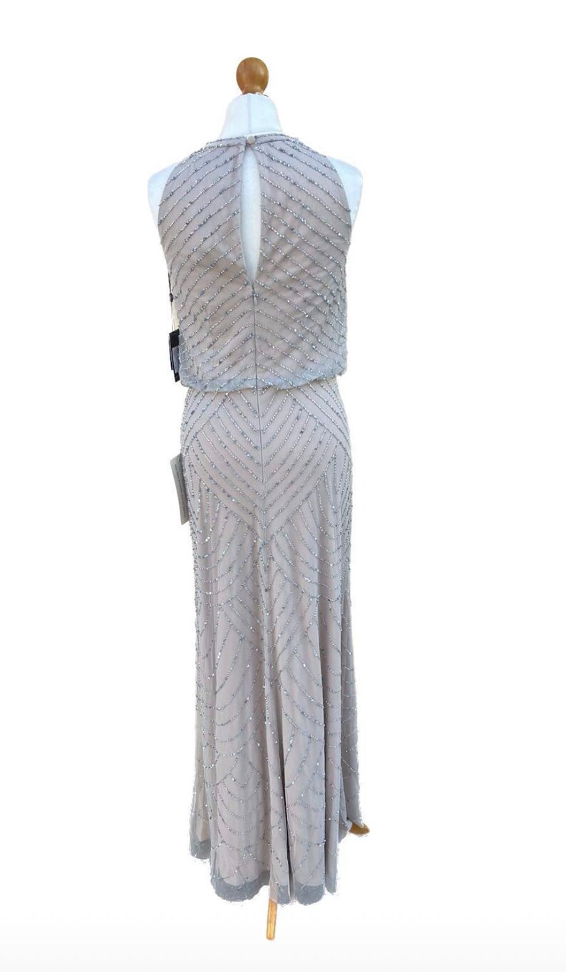 May include: A silver sequined halter dress with a geometric pattern. The dress has a keyhole back and a fitted bodice. The skirt is a-line and falls to the floor.