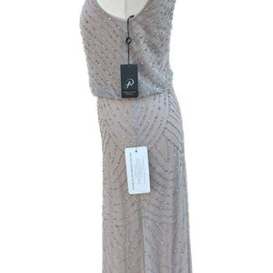 May include: A gray sleeveless maxi dress with a beaded pattern. The dress has a scoop neck and a fitted bodice. The dress is on a mannequin and has a tag that says "Adrianna Papell".