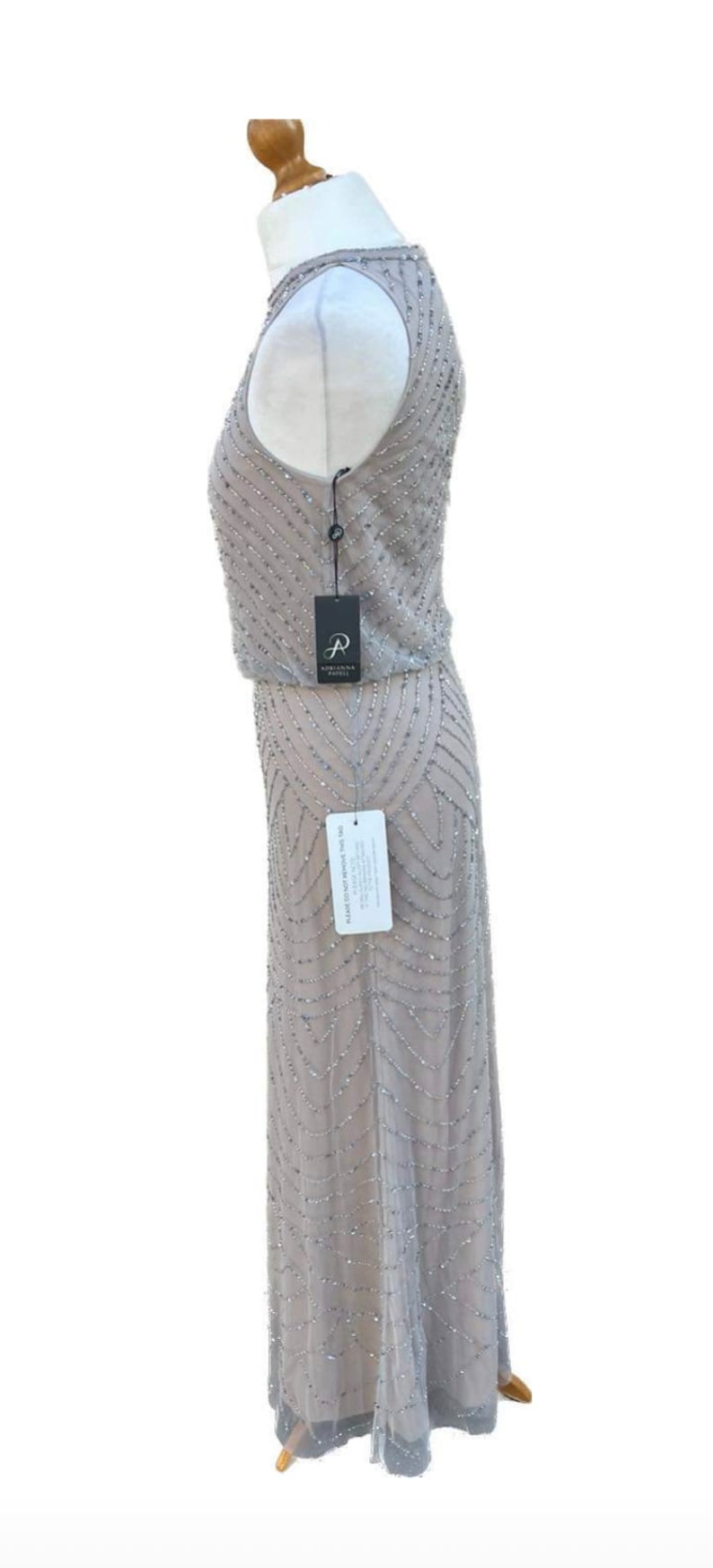 May include: A gray sleeveless maxi dress with a beaded pattern. The dress has a scoop neck and a fitted bodice. The dress is on a mannequin and has a tag that says "Adrianna Papell".
