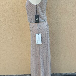 May include: A silver sequined maxi dress with a sleeveless design. The dress has a fitted bodice and a flowing skirt. The dress is on a mannequin and is displayed against a light beige wall.