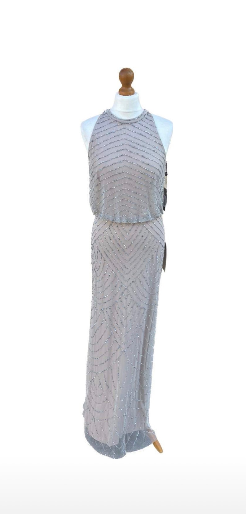 May include: A silver beaded halter-style dress with a geometric pattern. The dress is on a mannequin and has a simple, elegant design.