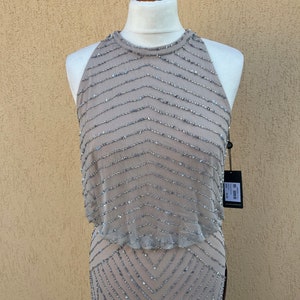 May include: A sleeveless, sequined dress in a light brown color with a geometric pattern. The dress has a halter neckline and a fitted silhouette.