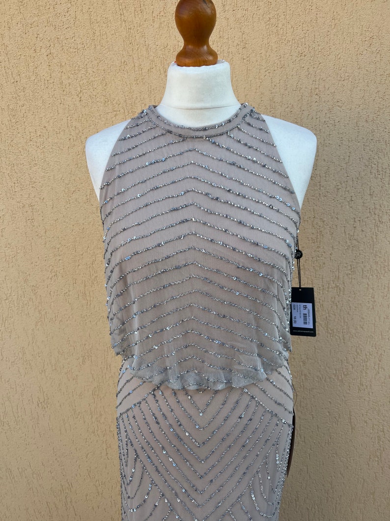 May include: A sleeveless, sequined dress in a light brown color with a geometric pattern. The dress has a halter neckline and a fitted silhouette.
