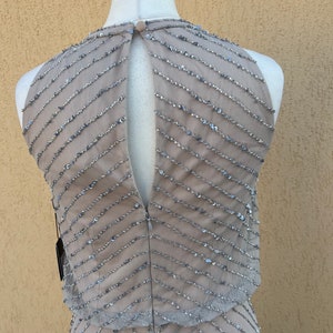 May include: A sleeveless, sequined dress in a light gray color with a geometric pattern. The dress has a keyhole back and a fitted silhouette.