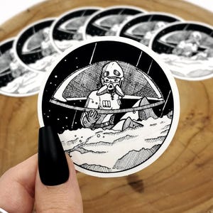 Puede incluir: Pegatinas redondas en blanco y negro. Cada pegatina presenta una ilustración detallada de una figura con casco y máscara, sobre un fondo estrellado. La figura está situada sobre un paisaje. Diseño artístico único.