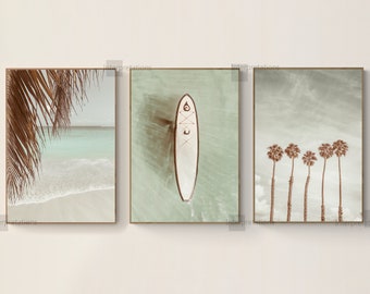 May include: Three framed prints with a beach theme. The first print shows a close-up of palm tree leaves and a beach with turquoise water. The second print shows a white paddleboard floating in turquoise water. The third print shows five palm trees against a light blue sky.