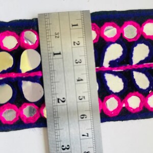 May include: A close-up of a blue and pink trim with mirrored embellishments. The trim is measured with a ruler, showing it is about 2 inches wide.