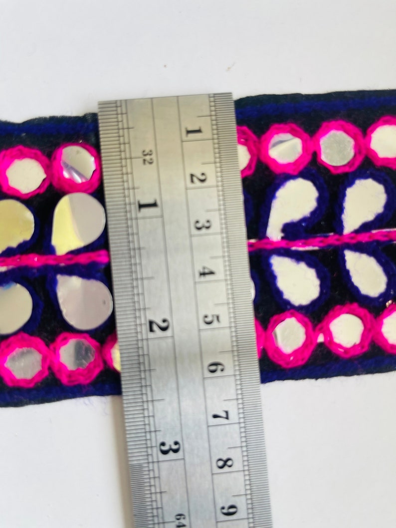 May include: A close-up of a blue and pink trim with mirrored embellishments. The trim is measured with a ruler, showing it is about 2 inches wide.
