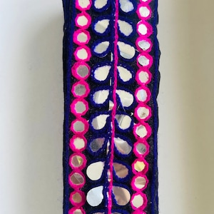 May include: A trim of black fabric with pink and blue embroidery and silver mirrored embellishments in the shape of leaves and circles.