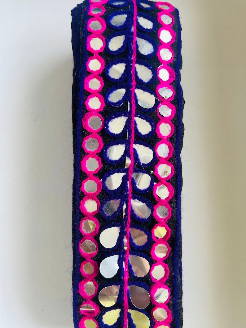 May include: A trim of black fabric with pink and blue embroidery and silver mirrored embellishments in the shape of leaves and circles.