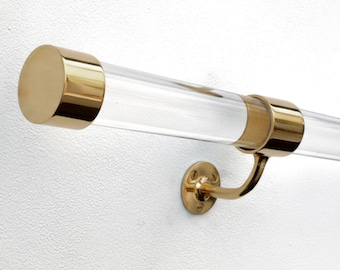 May include: A clear acrylic handrail featuring polished brass end caps and a matching brass wall-mounted bracket. The cylindrical rod is transparent, providing a sleek look, while the metallic hardware components offer a reflective gold finish.