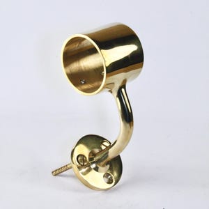 Puede incluir: Un soporte de pasamanos de latón pulido, con un brazo curvo y una placa de montaje circular. El soporte tiene una copa cilíndrica para el pasamanos y un tornillo para la instalación. El acabado es dorado brillante.