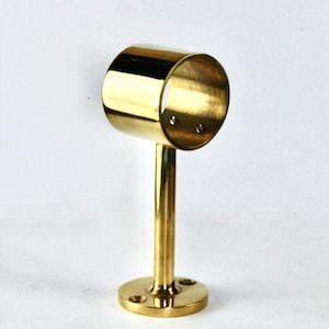 Puede incluir: Soporte de barra de cortina de latón dorado. Cuenta con un anillo cilíndrico, un vástago vertical y una base circular. El soporte está diseñado para montaje en pared. Diámetro de la base: aproximadamente 5 cm.