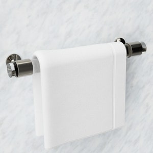 Op de afbeelding: Een witte handdoek hangt aan een zilveren handdoekrek dat aan een witte marmeren muur is gemonteerd.