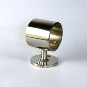 Könnte beinhalten: Ein glänzender, silberfarbener Gardinenstangenhalter. Der Halter hat eine kreisförmige Basis mit einem kurzen, vertikalen Pfosten, der einen zylindrischen Ring trägt. Das Metall hat eine polierte Oberfläche.