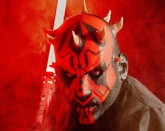 May include: A person wearing a red and black Darth Maul mask holds a white lightsaber in a red smoky background.