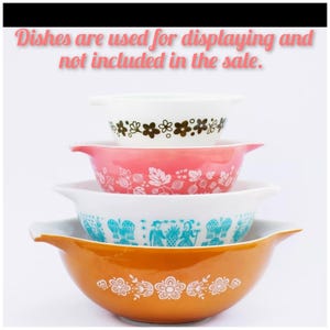 May include: A stack of four vintage Pyrex mixing bowls. The bowls are white, pink, turquoise, and orange, each with a different floral or patterned design. The text at the top says "Dishes are used for displaying and not included in the sale."