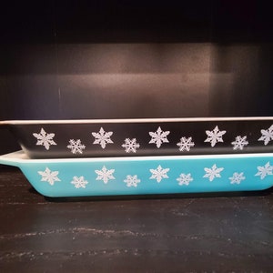 May include: Two vintage Pyrex baking dishes, one black with white snowflake design and one turquoise blue with white snowflake design.